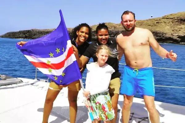Família a bordo de um catamarã segurando a bandeira de Cabo Verde durante um passeio de barco