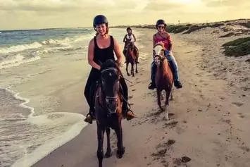 Turistas a passear a cavalo ao longo de uma praia de Cabo Verde ao entardecer